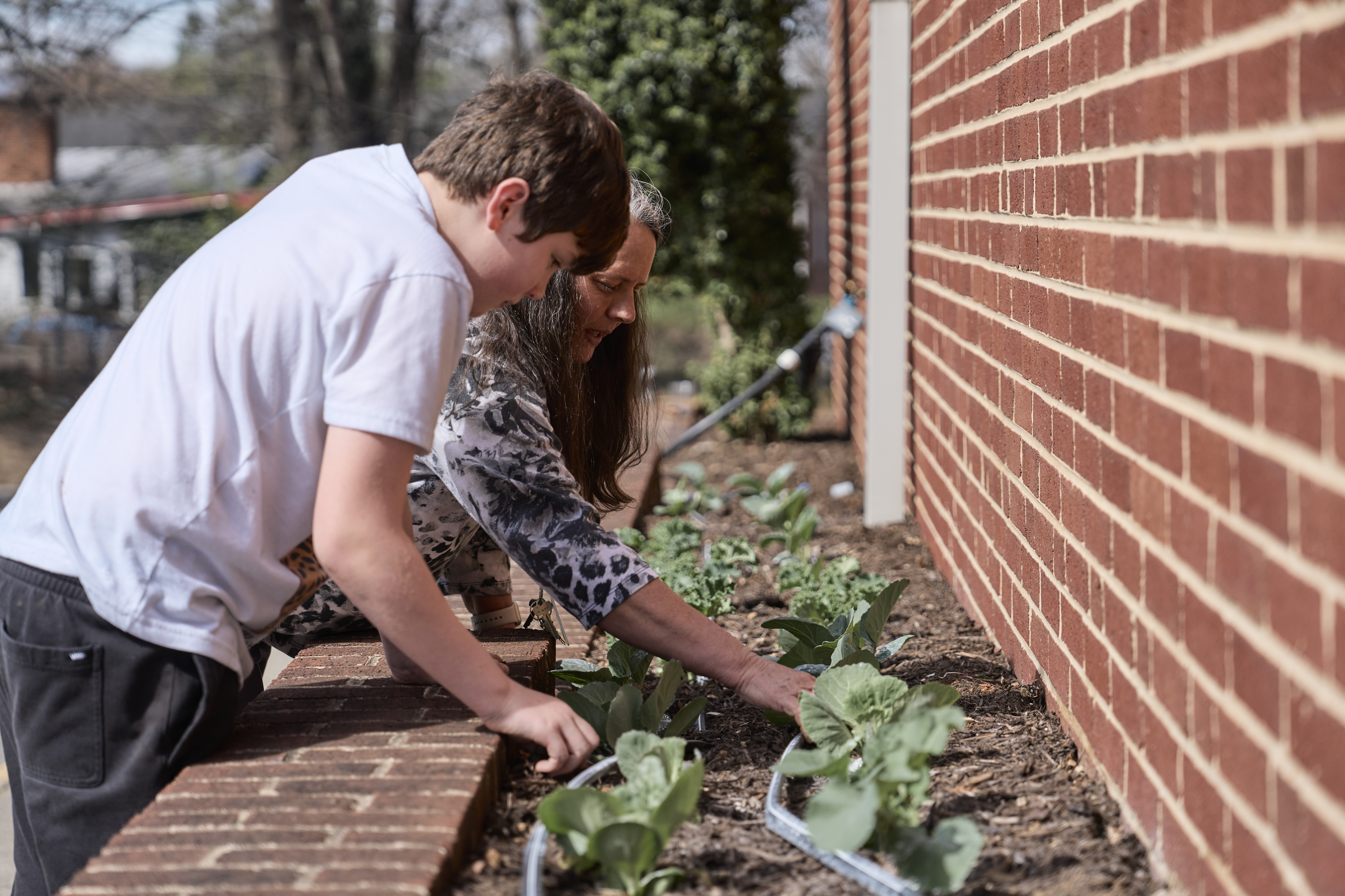 A student works with his teacher in the class garden.